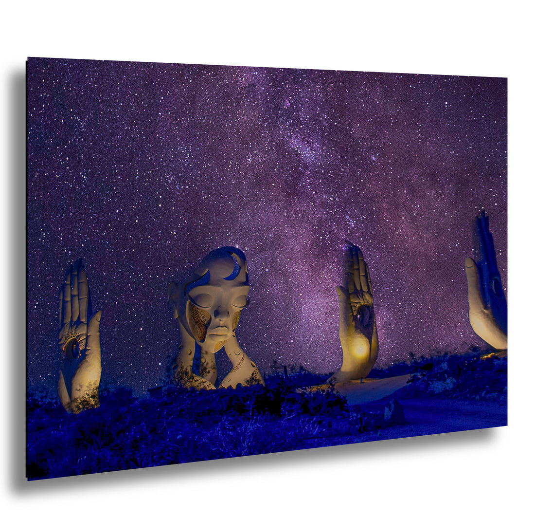 Surreal night sky with the Milky Way, featuring giant sculptures of a woman’s face and hands, illuminated under the stars in a desert landscape.