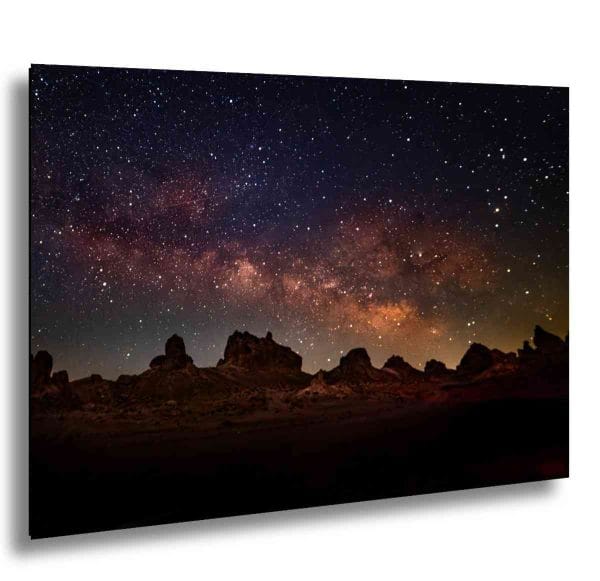 Milky Way galaxy over desert rock formations at night in vivid orange and purple.