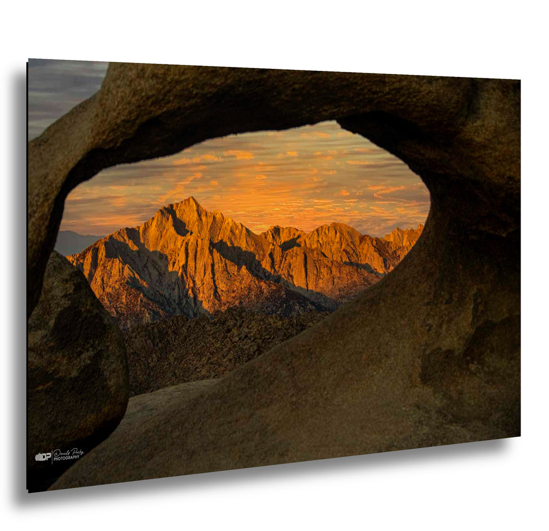 Joshua Tree National Park sunset framed through granite rock window with golden mountain peaks and orange sky.