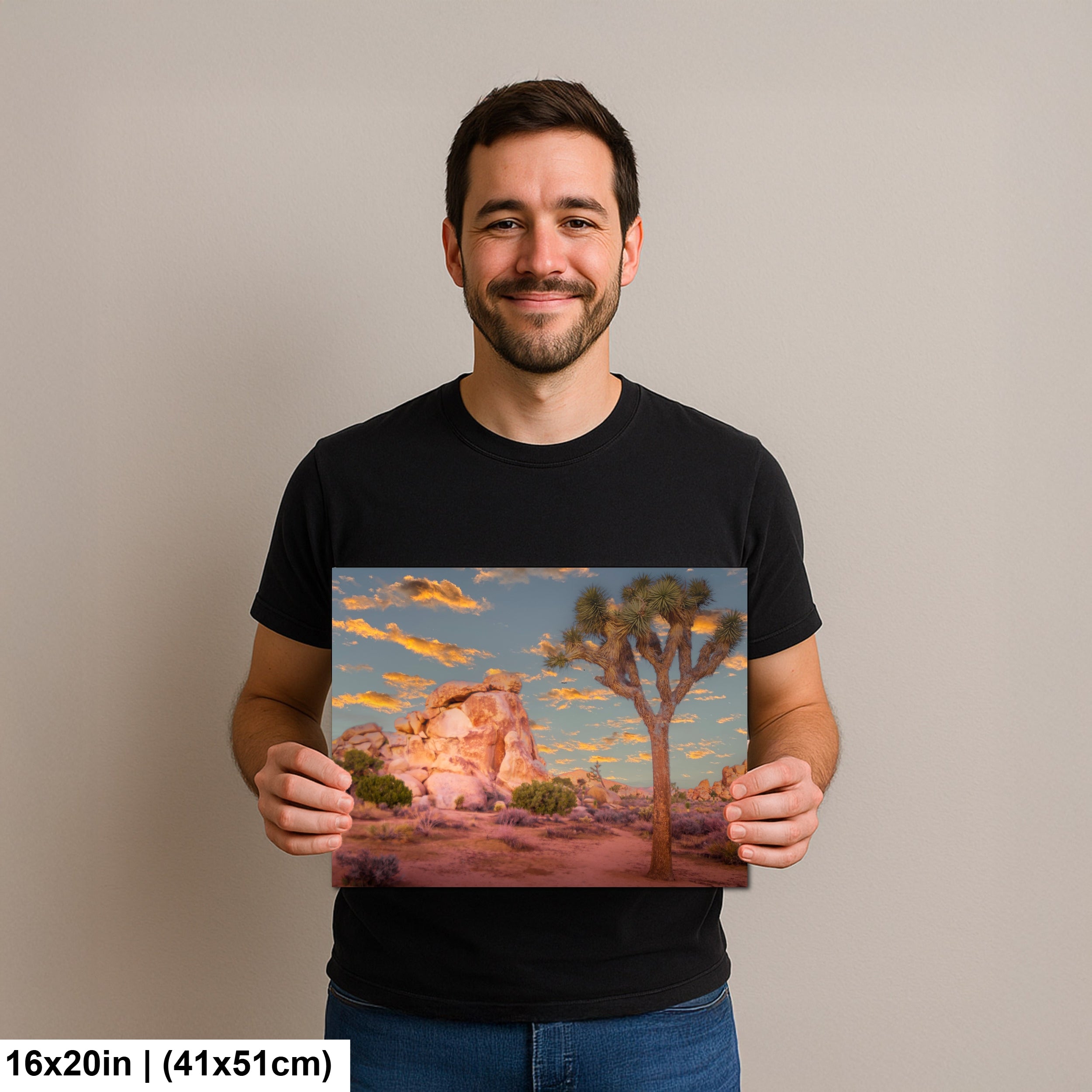 Man holding Joshua Tree National Park sunset photography print with pink boulders and orange sky landscape art.