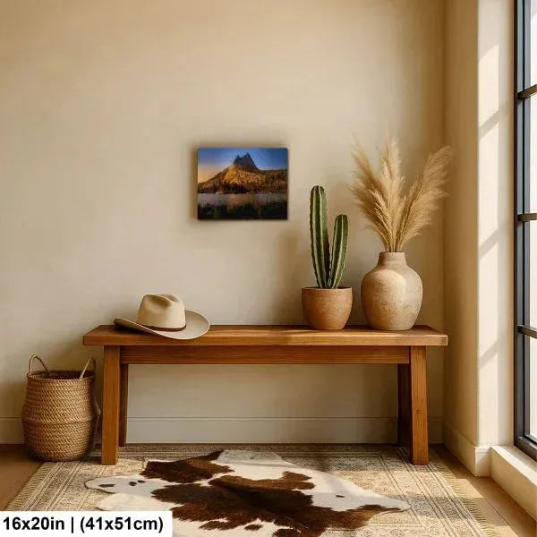 Cozy entryway with a wooden bench, potted plants, a cowhide rug, and a mountain landscape print hanging above, bathed in natural sunlight.