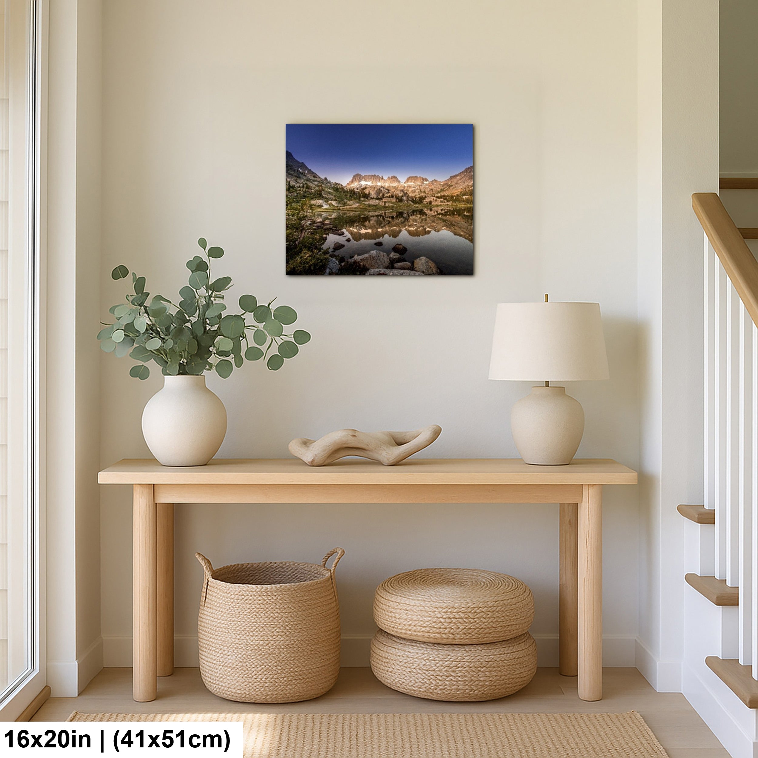 Mountain lake reflection landscape canvas above wooden console table with eucalyptus and woven baskets in minimalist home decor.