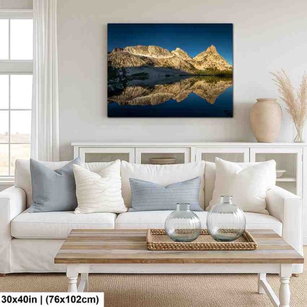 Snow-capped mountain peaks reflected in alpine lake canvas above white sofa in coastal farmhouse living room.