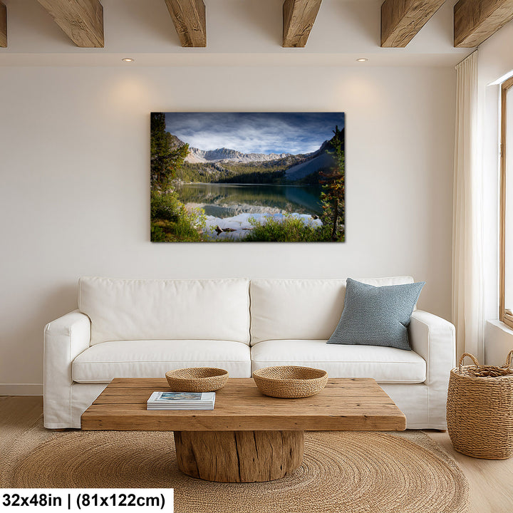 Alpine lake reflection with granite mountains and forest canvas above white sofa in modern farmhouse living room.