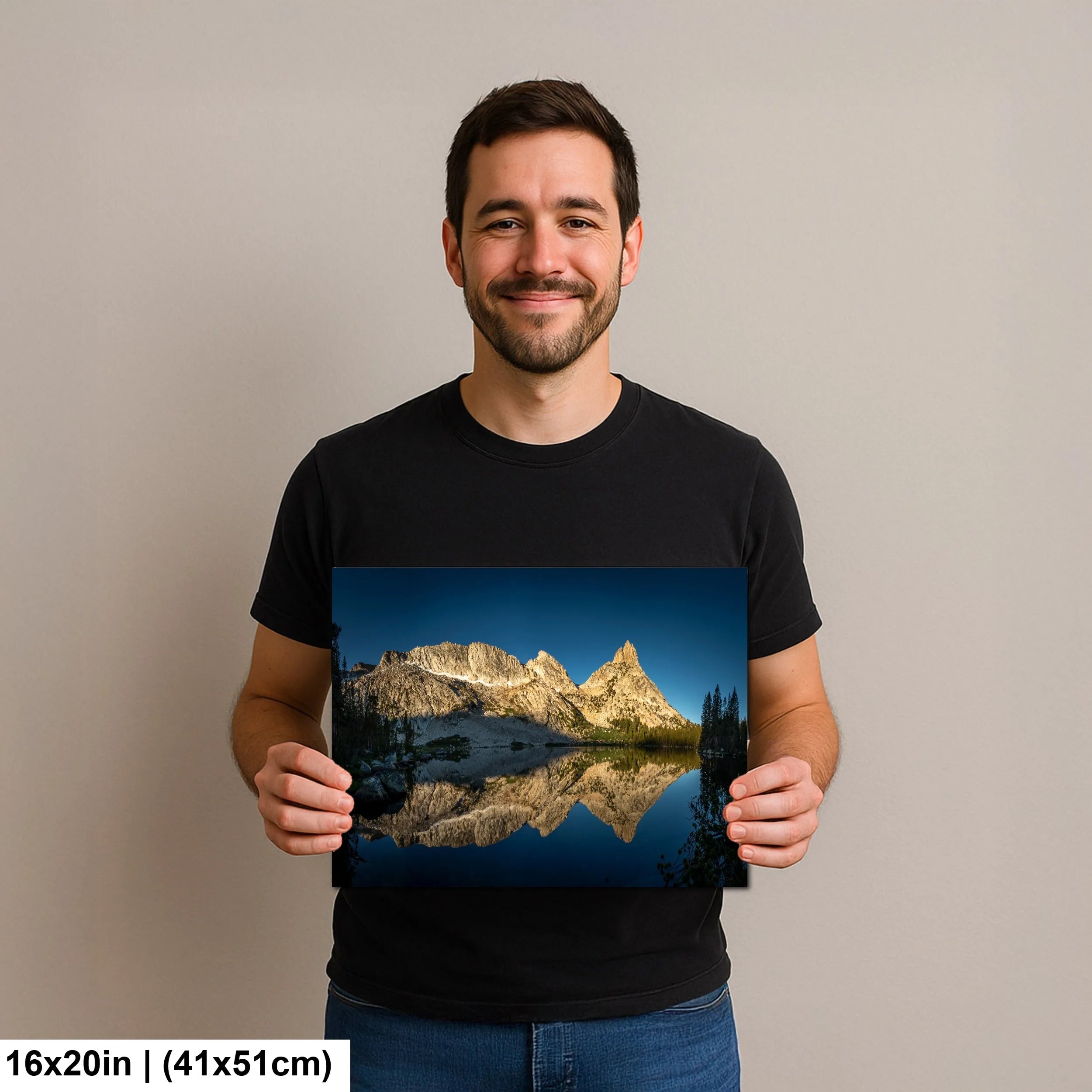 Man holding a 6x20 inch print of a mountain landscape with its reflection in a tranquil lake, smiling against a neutral background.