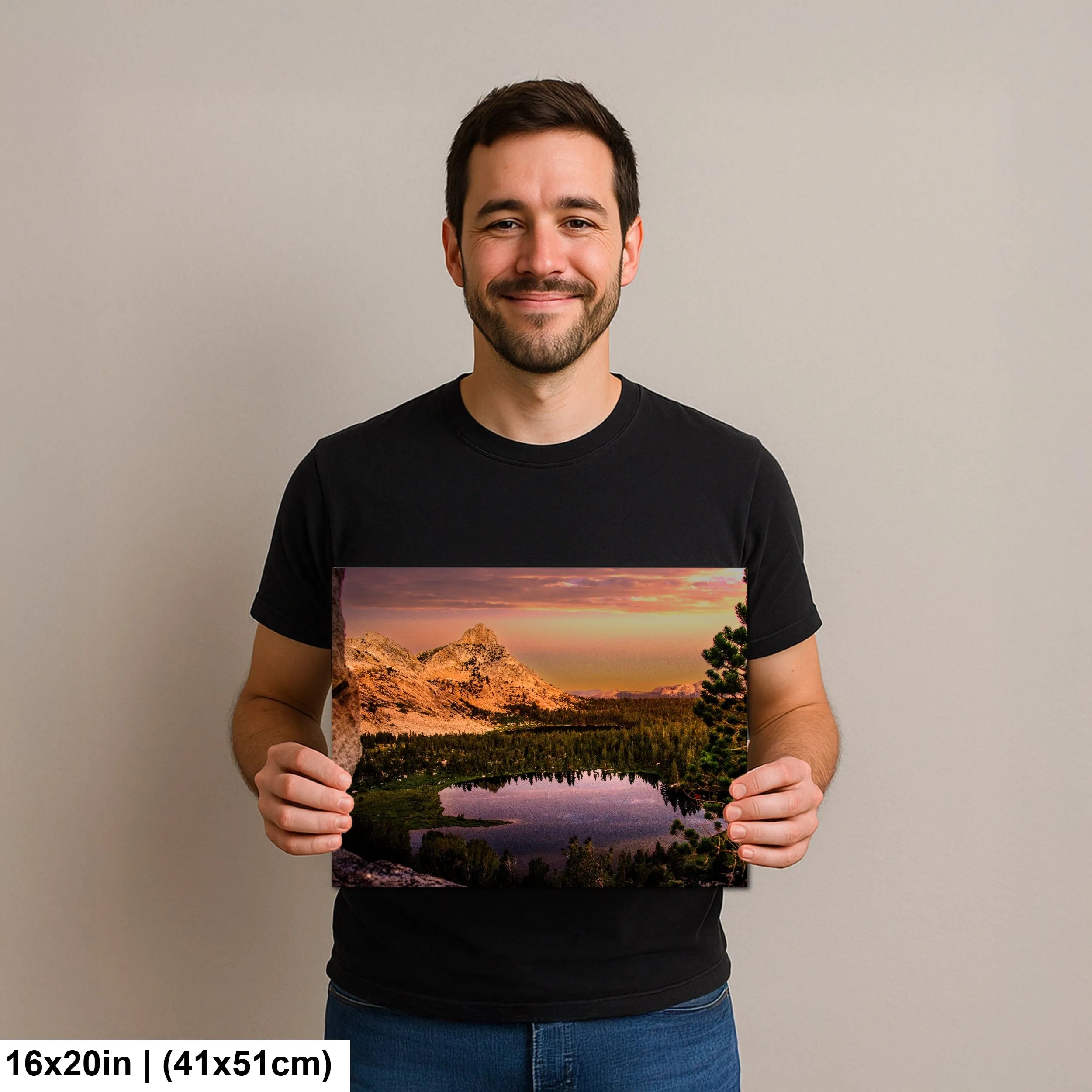 Man holding a 16x20 inch print of a serene mountain landscape featuring a tranquil lake and lush greenery under a soft sunset sky.